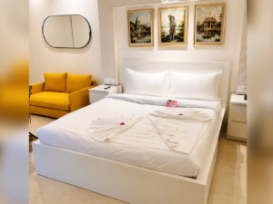 Well-furnished studio bedroom with a plush king bed, yellow sofa, and devotional artwork at Vrindavan Staycation.