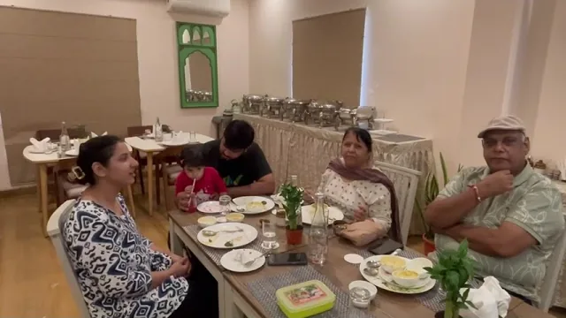 Video still: a family of five around a table in the dining hall