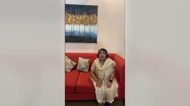 Video still: a guest seated on the red sofa in the lounge, speaking to the camera