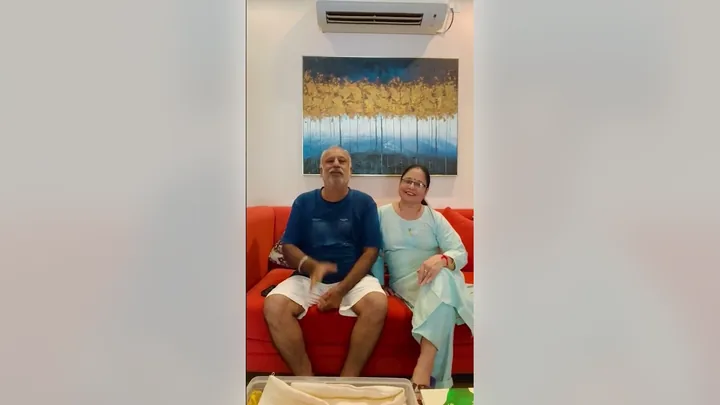 Video still: a couple seated together on the red sofa in the lounge