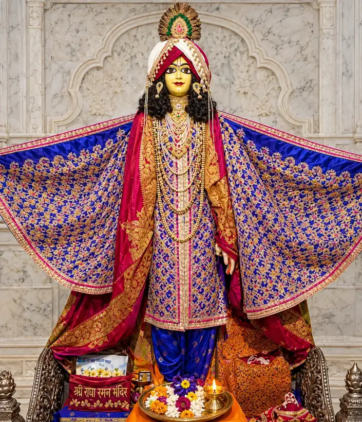 The deity of Shri Chaitanya Mahaprabhu at the Amiya Nimai Mahaprabhu Temple, Vrindavan: golden-faced, in a crimson turban with a jewelled crown, robed in blue and gold brocade with arms outspread, before a carved white marble wall